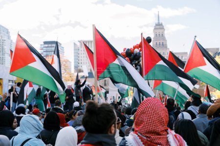 Foto de Un mar de manifestantes ondeando banderas palestinas se reúne en un entorno urbano con una torre de reloj histórica a lo lejos, mostrando unidad y solidaridad. Foto de alta calidad - Imagen libre de derechos