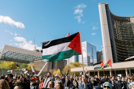 Foto de Toronto, Canadá - 28 de octubre de 2023: Manifestantes se reúnen en una plaza de la ciudad, ondeando banderas palestinas en medio de rascacielos modernos bajo un cielo azul claro. Foto de alta calidad - Imagen libre de derechos
