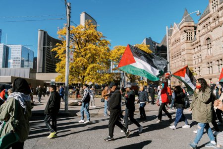 Photo for Anti-war march in Toronto by Palestinians against Israels aggression in Gaza. Citys peaceful protest against Israel-HAMAS war. Protesters wave flags against. Palestinian genocide. - Royalty Free Image