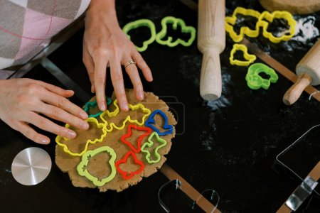 Foto de El confitero distribuye cortadores de galletas multicolores sobre la masa sobre la mesa. Cultivado. Foto de alta calidad - Imagen libre de derechos