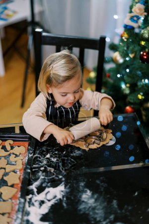 Foto de La niña pone en marcha cortadores de galletas en una masa con un pequeño rodillo. Foto de alta calidad - Imagen libre de derechos