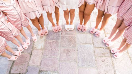 Bride and bridesmaids stand in pajamas and slippers on the tiles in a semicircle. Cropped. Faceless. High quality photo