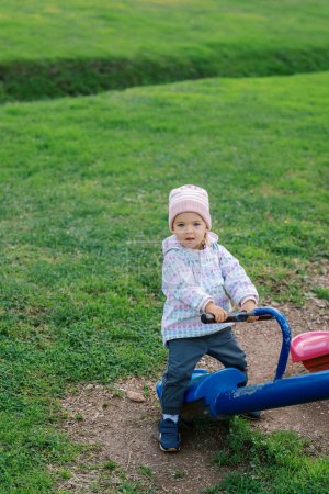 Foto de La niña está de pie sobre el asiento de un balanceador, agarrándose a la manija. Foto de alta calidad - Imagen libre de derechos