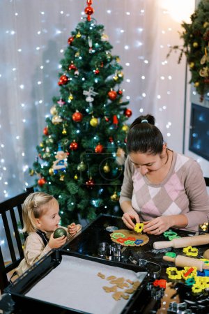 Foto de La niña mira a su madre cortando galletas con cortadores de galletas de colores en la mesa. Foto de alta calidad - Imagen libre de derechos