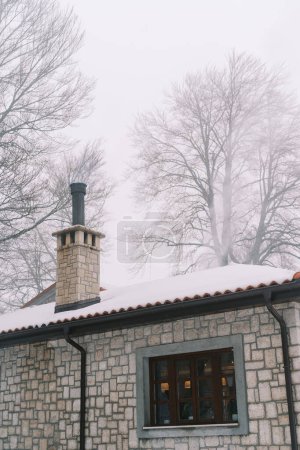 Foto de Acogedora casa de piedra en un bosque de invierno con una chimenea alta. Foto de alta calidad - Imagen libre de derechos