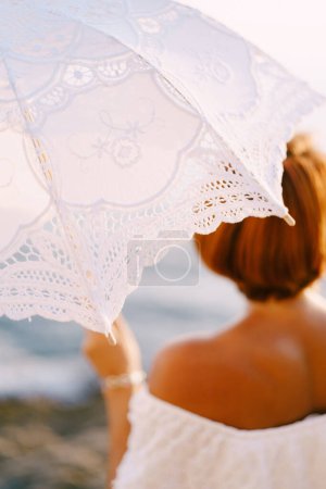 Téléchargez les photos : Parapluie solaire ajouré blanc dans la main d'une femme au bord de la mer. Photo de haute qualité - en image libre de droit