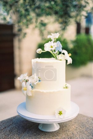 Foto de Pastel de boda de dos niveles decorado con flores se encuentra en una bandeja sobre la mesa. Foto de alta calidad - Imagen libre de derechos