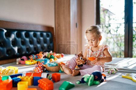 Photo for Little girl plays with a plush deer on the bed among colorful soft toys. High quality photo - Royalty Free Image