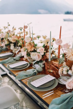 Téléchargez les photos : Des menus festifs se trouvent sur des assiettes près de bougies et de bouquets de fleurs sur une table en bois. Photo de haute qualité - en image libre de droit