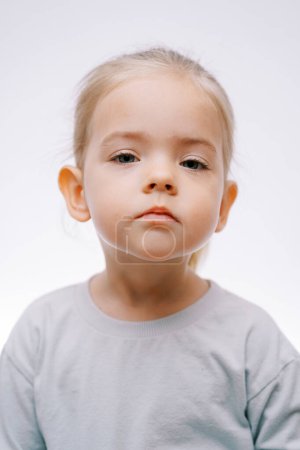 Téléchargez les photos : Portrait d'une petite fille triste et sérieuse sur fond gris. Photo de haute qualité - en image libre de droit