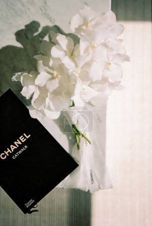 Téléchargez les photos : Bouquet freesia blanc se trouve sur une table en marbre à côté d'un livre. Cartouche : Chanel. Passerelle. Photo de haute qualité - en image libre de droit