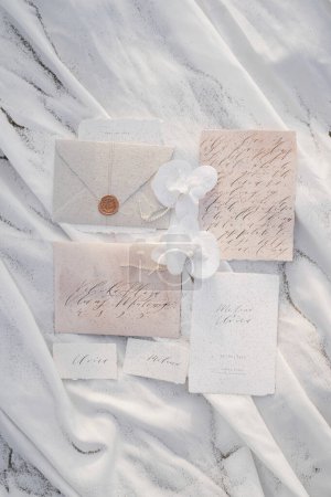 Photo for Wedding invitations with name cards lie next to envelopes and flowers on a white cloth. High quality photo - Royalty Free Image