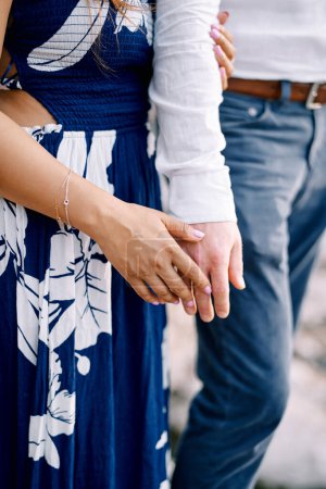 Woman stands, hugging man arm and touching his palm with her palm. Cropped. Faceless. High quality photo