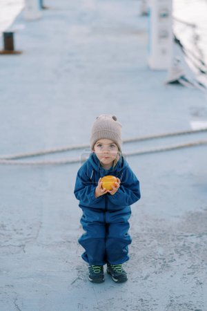 Little girl in overalls with a ripe persimmon in her hands squatted on the road. High quality photo