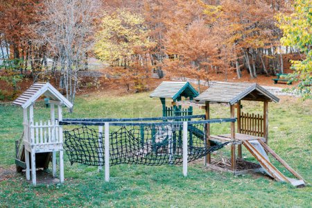 Wooden playground in the autumn forest with slides and agility mesh bridge. High quality photo