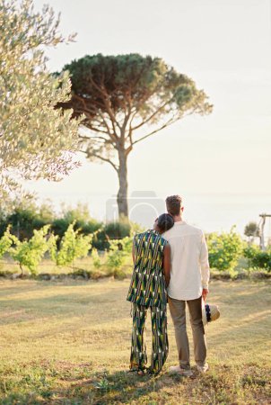 Woman rested her head on man shoulder while standing with him in a green garden. Back view. High quality photo