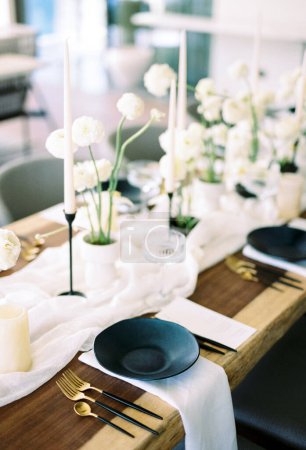 Téléchargez les photos : Des assiettes noires se dressent sur des serviettes blanches à côté de bouquets de fleurs et de bougies sur la table de fête. Photo de haute qualité - en image libre de droit