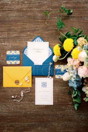 Photo for Wedding invitations with blue and yellow envelopes, name cards and a bouquet of flowers lie on a wooden table. High quality photo - Royalty Free Image
