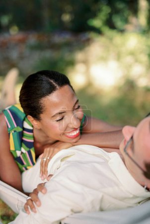 Lächelnde Frau, die ihren Kopf auf die Hand auf der Brust eines Mannes legt, der in einer Hängematte liegt. Hochwertiges Foto
