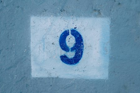 Número nueve dibujado en una pared azul rayada en un rectángulo blanco. Foto de alta calidad