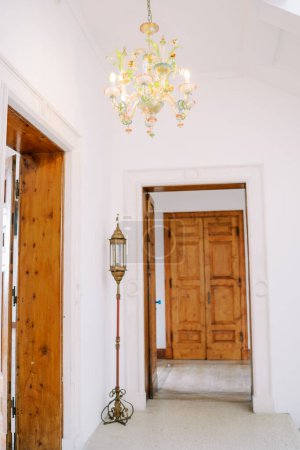 Lámpara de araña de colores con decoraciones florales y colgantes cuelga en el techo cerca de una puerta de madera en una habitación. Foto de alta calidad