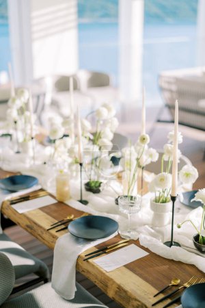 Téléchargez les photos : Des assiettes noires sur des serviettes blanches se trouvent à côté de couverts en or et de menus sur une table de vacances avec des fleurs blanches. Photo de haute qualité - en image libre de droit