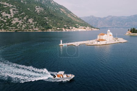 Motorboat sails on the sea past the Church of Our Lady on the Rocks of the island of Gospa od Skrpjela. Montenegro. Drone. High quality photo