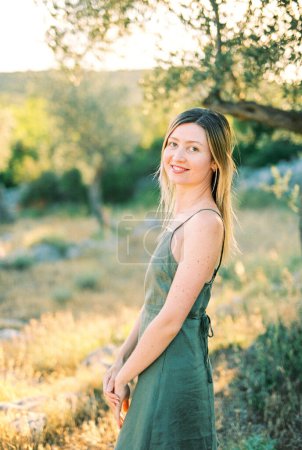 Smiling young woman stands half-turned near a tree. High quality photo