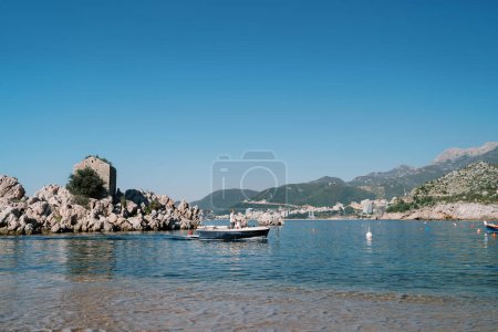 El hombre navega un barco de pesca más allá de una isla frente a la costa montañosa. Przno, Montenegro. Foto de alta calidad