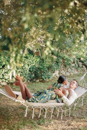 Smiling man hugs the waist of woman lying on him in a hammock in a green garden. High quality photo