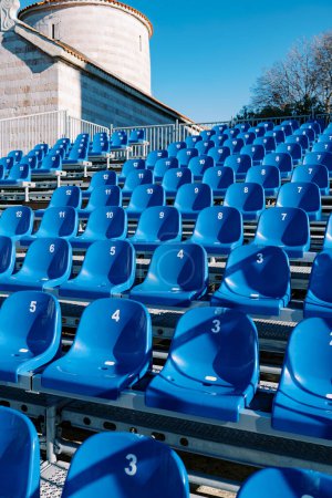 Téléchargez les photos : Des rangées de sièges bleus dans un stade près d'une ancienne église. Photo de haute qualité - en image libre de droit