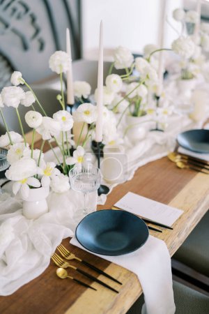 Téléchargez les photos : Les menus se trouvent près des assiettes noires sur une table festive avec des fleurs blanches sur une nappe étroite. Photo de haute qualité - en image libre de droit