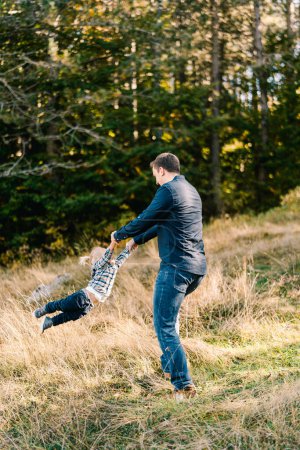 Dad is circling a little girl by the arms on a sunny lawn in the forest. High quality photo
