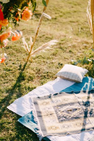 Selbstgemachte Tagesdecken neben Kissen liegen auf einem grünen Rasen in der Nähe des Wedding-Pergwam-Bogens. Hochwertiges Foto