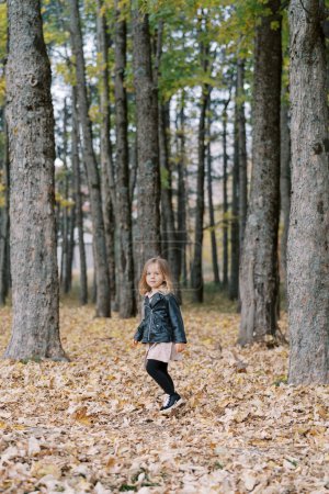 Petite fille marche à travers un tapis épais de feuilles sèches tombées dans la forêt d'automne. Photo de haute qualité