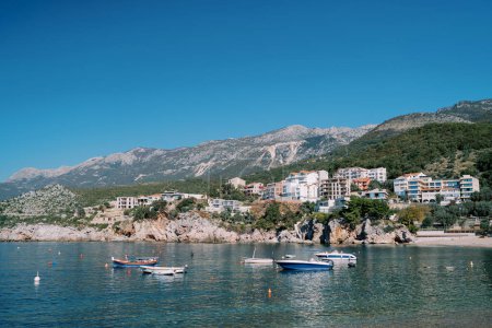 Barcos de pesca están amarrados en el mar cerca de coloridos hoteles en una ladera rocosa. Przno, Montenegro. Foto de alta calidad