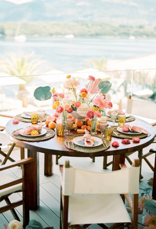 Foto de Mesa redonda festiva con ramos de flores y platos en alfombras de mimbre en la terraza con vistas al mar. Foto de alta calidad - Imagen libre de derechos
