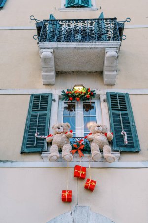 Große Teddybären sind an einem Fensterbrett an der Fassade eines Gebäudes befestigt und weihnachtlich dekoriert. Hochwertiges Foto