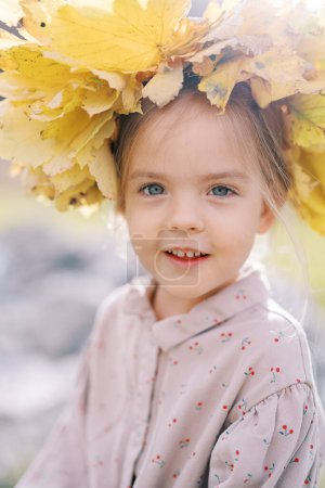 Kleines geheimnisvoll lächelndes Mädchen in einem Kranz aus gelben Blättern. Porträt. Hochwertiges Foto