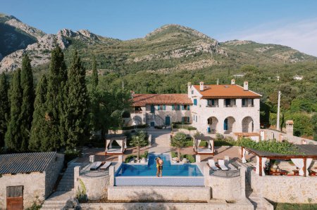 Man and woman stand hugging and kissing on the edge of a swimming pool near an old villa at the foot of the mountains. High quality photo