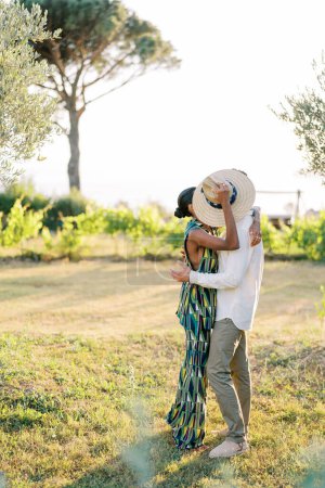 Man kisses woman while standing in a green garden and hiding behind a straw hat. High quality photo