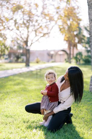 Mom squatted down next to a little smiling girl in a sunny meadow. High quality photo