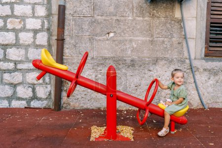 Foto de La niña se sienta en un balanceador cerca de una casa vieja y mira hacia otro lado. Foto de alta calidad - Imagen libre de derechos