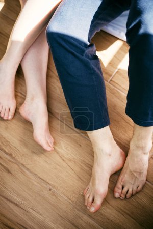 Bare feet of man and woman sitting on a wooden floor. Cropped. Faceless. High quality photo