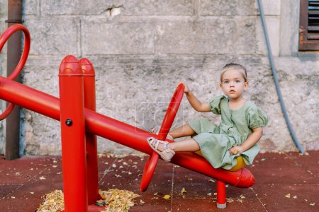 Foto de Niña sentada en un balanceador de swing sosteniendo una manija en un patio de recreo. Foto de alta calidad - Imagen libre de derechos