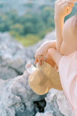 Eine junge Frau mit Hut in der Hand sitzt auf einem Felsen und legt ihr Kinn auf die Hand. Beschnitten. Hochwertiges Foto