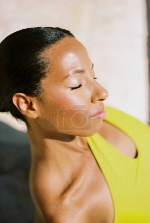 Une jeune femme prend un bain de soleil en étant assise les yeux fermés. Gros plan. Photo de haute qualité