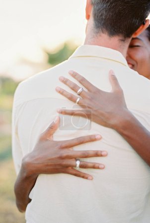 Smiling woman hugs man back, touching his neck with her nose. Back view. High quality photo