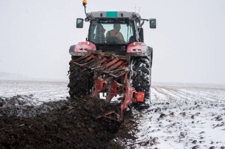 Foto de El tractor está trabajando en el campo, preparando el suelo en invierno para la siembra de primavera. Cultivo de tierras cultivables. - Imagen libre de derechos
