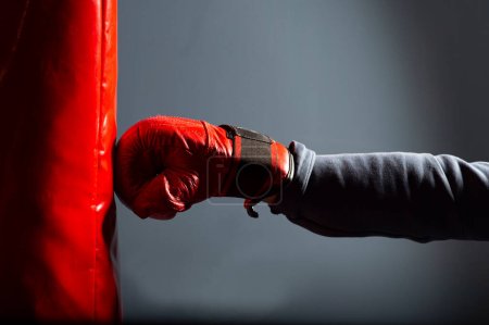 Foto de Practicando golpes en un saco de boxeo en el gimnasio. En primer plano, un guante rojo y un saco de boxeo rojo. - Imagen libre de derechos